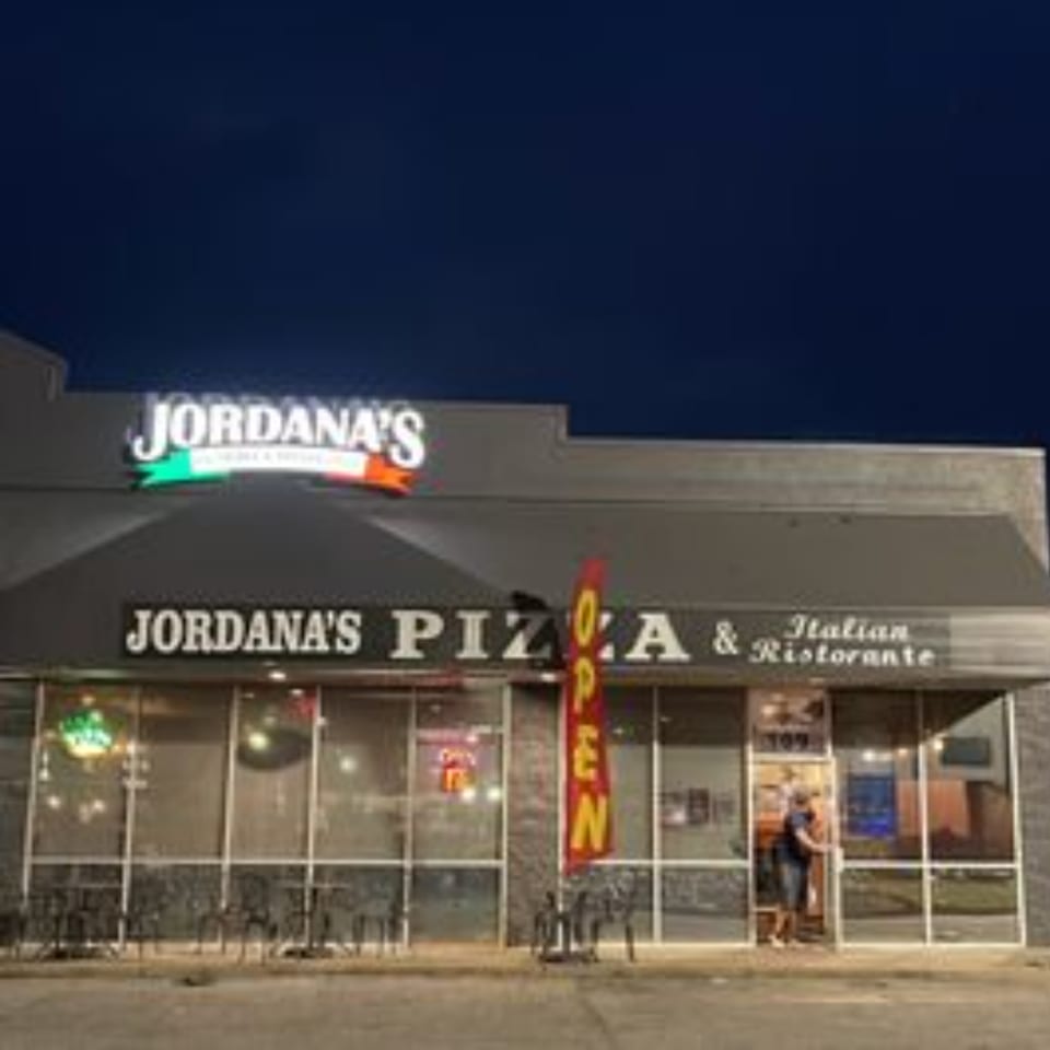 Jordana's Pizzeria & Italian Ristorante exterior at dusk, with illuminated signs and a person entering.