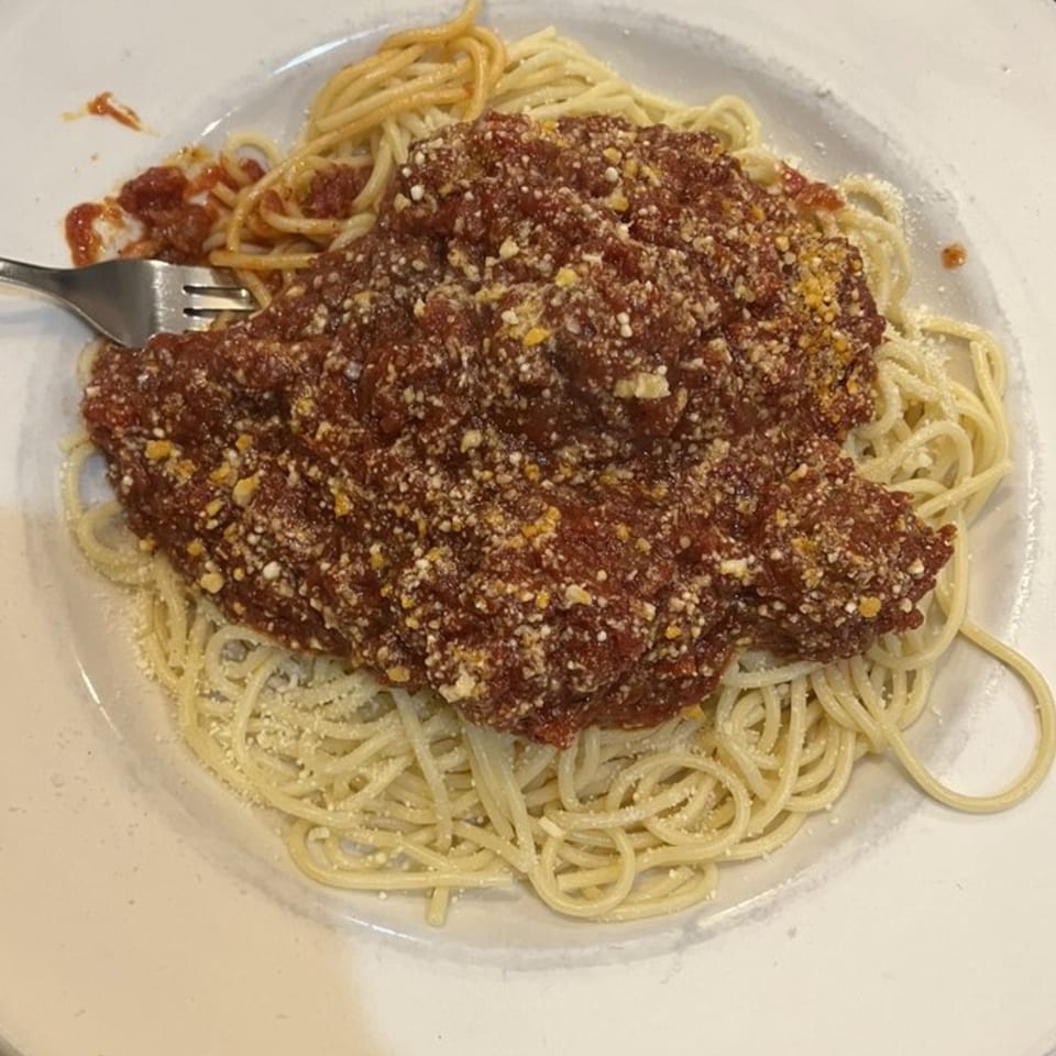 A plate of spaghetti with a generous serving of meat sauce and grated cheese, with a fork.