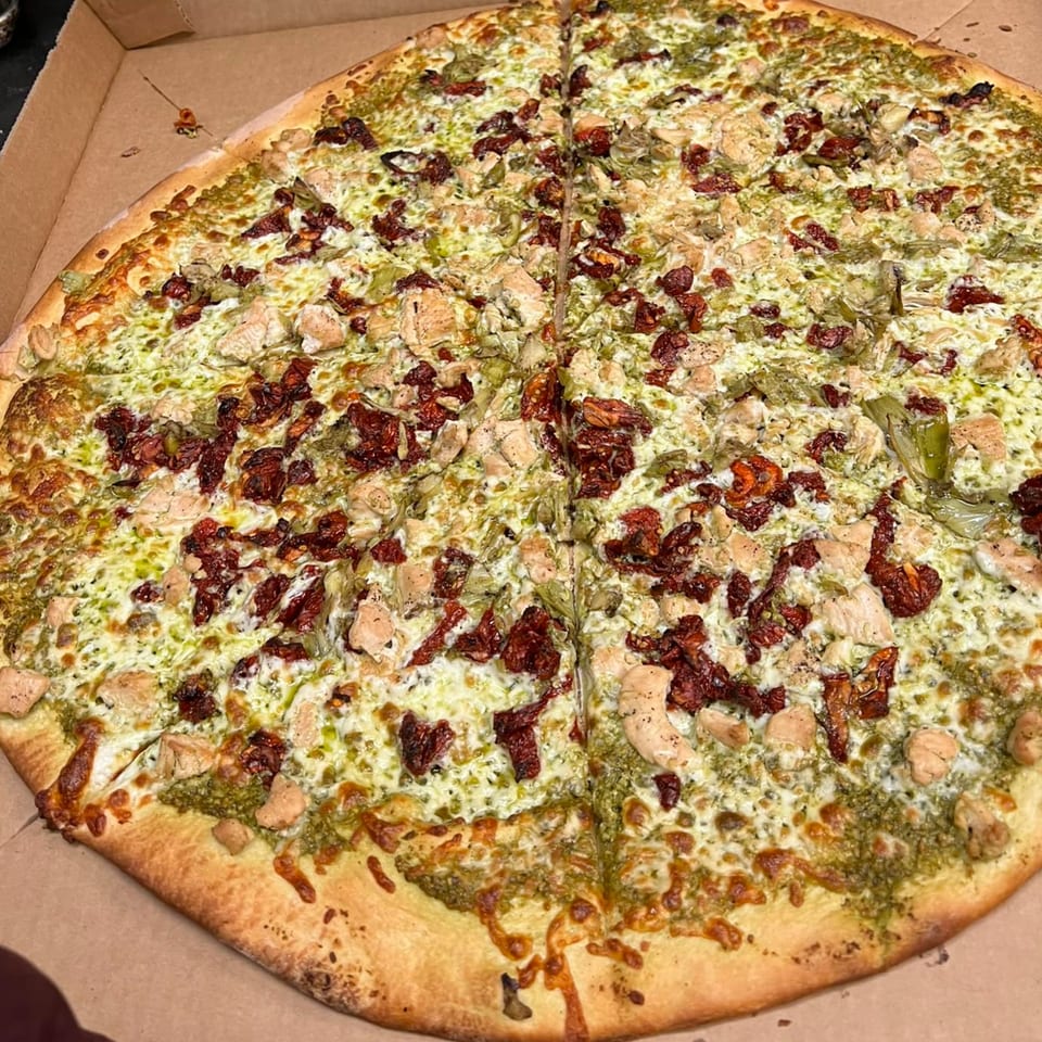 A large, round Jordana's Pizzeria pizza with pesto, white cheese, chicken, and sun-dried tomatoes.