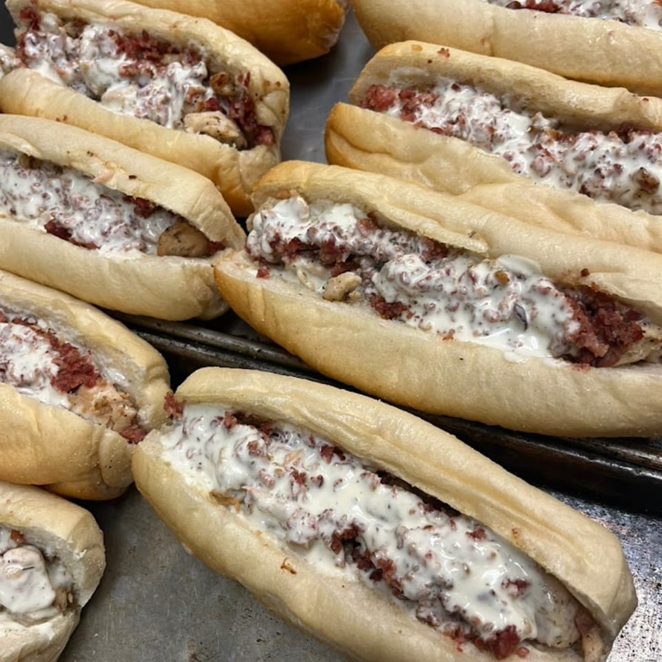 Several Italian subs with creamy white sauce and red meat crumbles on a metal tray.