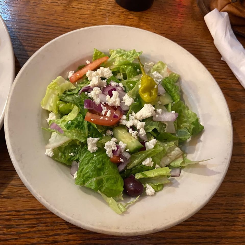 A fresh Italian salad with lettuce, tomatoes, red onion, feta cheese, olives, and a pepperoncini.