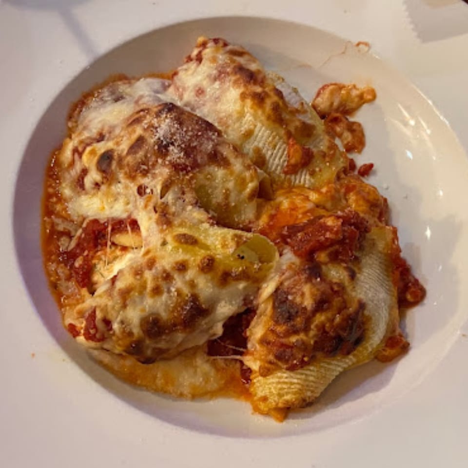 Baked stuffed shells with melted cheese and red sauce on a white plate at Jordana's Pizzeria.