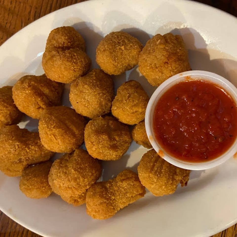A plate of golden-brown fried mushrooms with a side of red marinara dipping sauce.